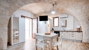 A compact kitchen with a dining area, stone walls, and a flat-screen TV. - Apartment 'Casa Sardella, Nel Centro Storico' with Wi-Fi and Air Conditioning (Monopoli)