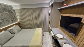 A modern hotel room with a large bed, a dining area with a table and chairs, and a TV mounted on the wall. - Melhores Flats - Excelente junto ao mar (João Pessoa)