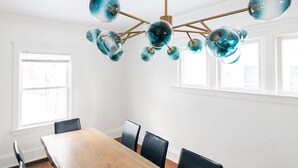Un espace de salle à manger moderne avec une table en bois et des chaises noires, un lustre sphérique original et de grandes fenêtres qui laissent entrer la lumière naturelle.