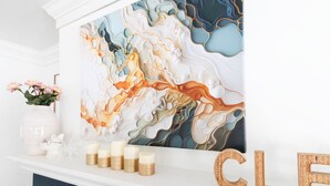 Une cheminée blanche ornée d’une grande peinture abstraite, d’un vase rempli de roses roses et d’un panneau indiquant « PROPRE ».