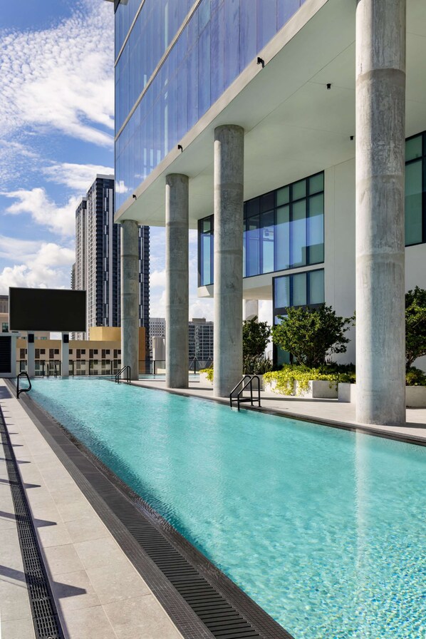 A modern building with a swimming pool, large windows, and concrete pillars.