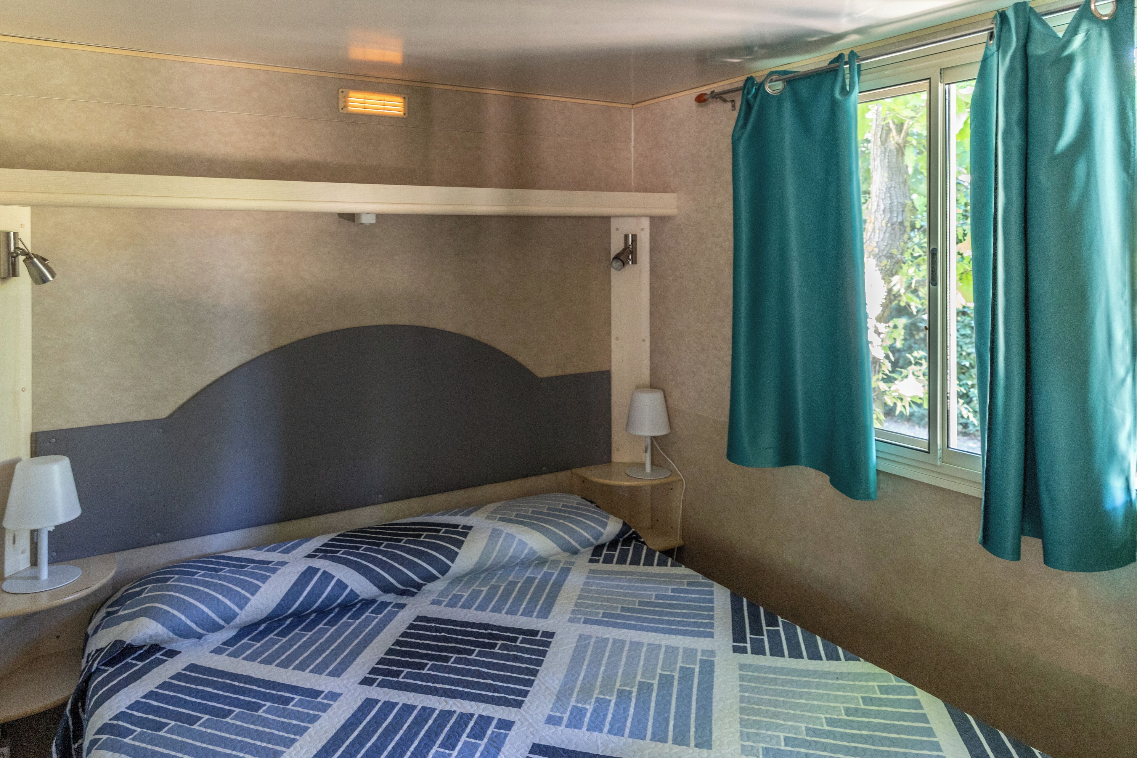 Ein Bett mit Kopfteil, ein Nachttisch mit Lampe und ein Fenster mit Vorhängen.