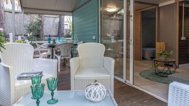 Ein überdachter Patio-Bereich mit Rattanmöbeln, einem Tisch mit grünem Glas und einer weißen, kugelförmigen Dekoration.