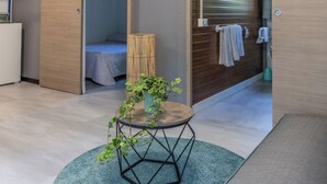 Ein modernes Hotelzimmer mit einem Bett, einem kleinen runden Tisch mit einer Pflanze, einem Bambuskorb und einem Handtuchhalter.