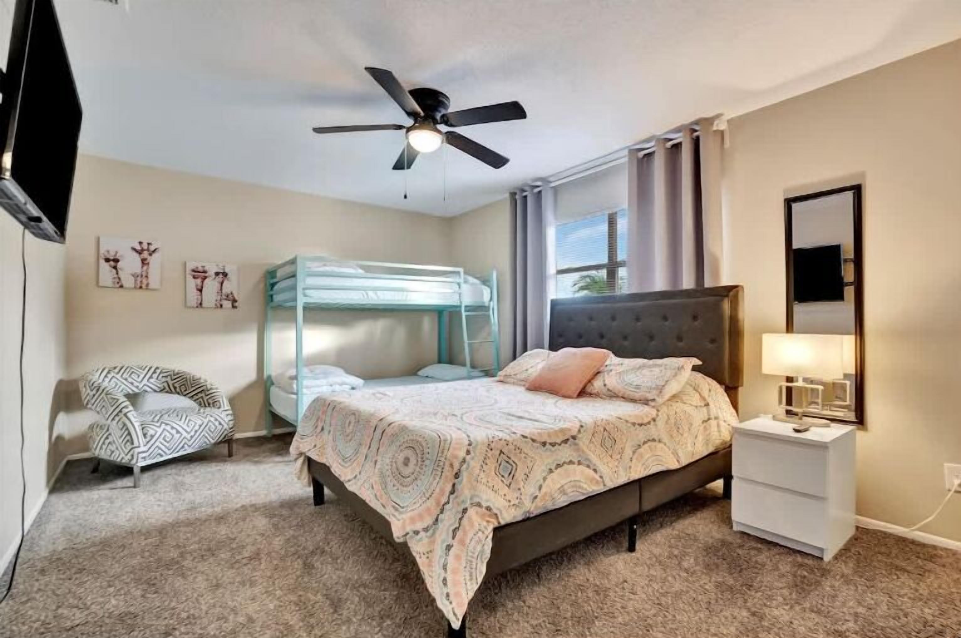 A bedroom with a bed, a nightstand, a chair, a ceiling fan, and artwork on the wall.