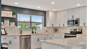 Una cocina moderna con armarios blancos, electrodomésticos de acero inoxidable y un ventanal que proporciona luz natural.