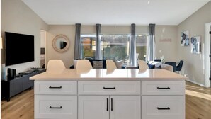 Una sala moderna con una isla grande, armarios blancos, un televisor de pantalla plana y un comedor con mesa y sillas.