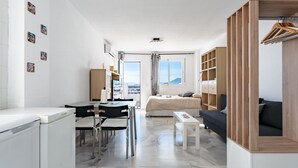A modern, compact room with a bed, a desk, a chair, a small table, and a wardrobe.
