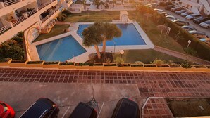 A resort with a swimming pool, multiple balconies, and a view of the sunset over the sea.
