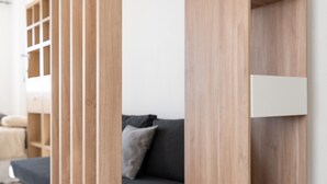 A modern living room with a dark sofa, wooden paneling, and a white cabinet.