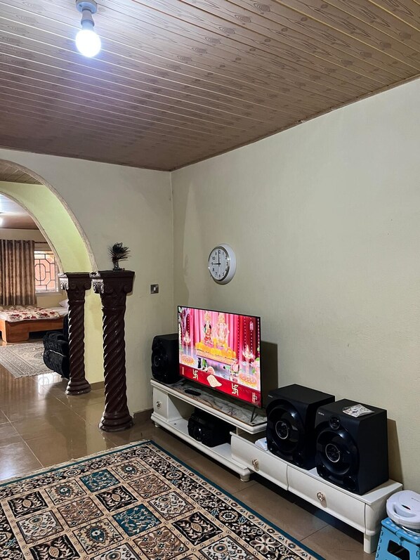 A living room with a television, speakers, a clock, and a patterned rug.
