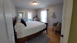A bedroom with a large bed, a nightstand, a chair, a dresser, a mirror, and a window with curtains.