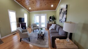A living room with a wooden ceiling, a grey sofa, a coffee table, and a TV on a stand.