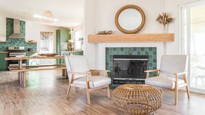 A modern living room with a fireplace, two armchairs, a round coffee table, and a kitchen in the background. - Joshua Tree-Spa Pool Firepit Sauna Game Room (Yucca Valley)