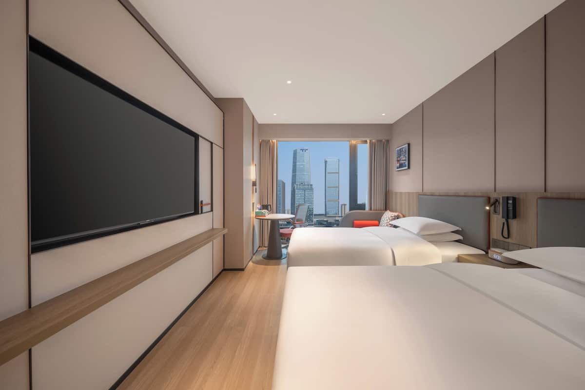 A hotel room with a large bed, a desk, a chair, a TV, and a view of the cityscape.