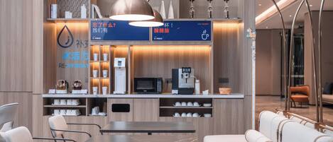 A modern hotel lobby with a reception desk, seating area, and amenities like a coffee machine and water dispenser.