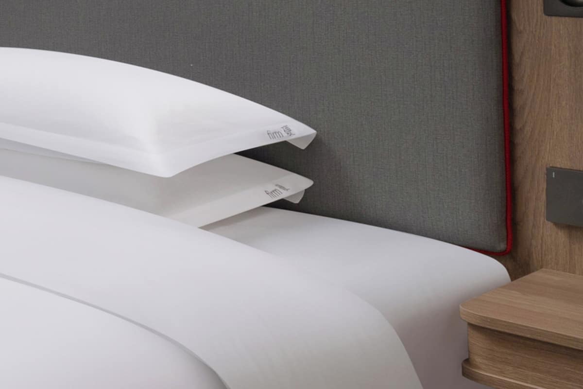 A neatly made bed with white linens and a wooden nightstand beside it.