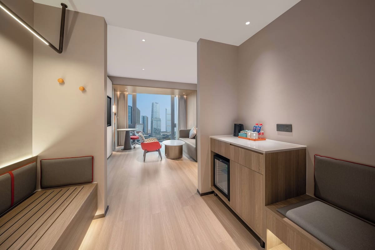A modern hotel room with a kitchenette, seating area, and a view of the city skyline.