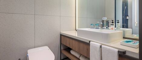 A modern bathroom with a white toilet, a large mirror, and a white sink with a wooden vanity.