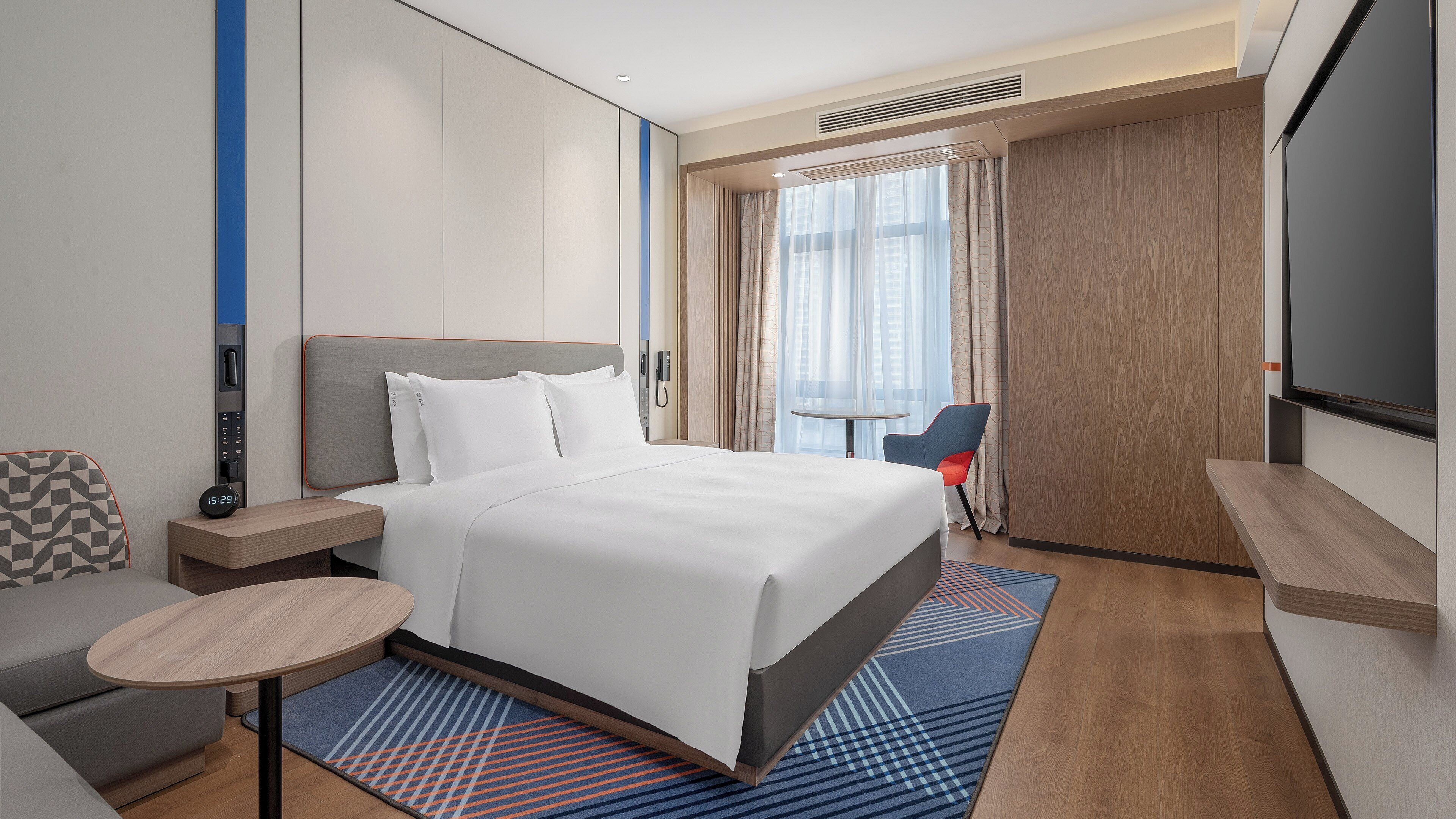 Une chambre d’hôtel moderne équipée d’un grand lit, d’un bureau, d’une chaise et d’un téléviseur.