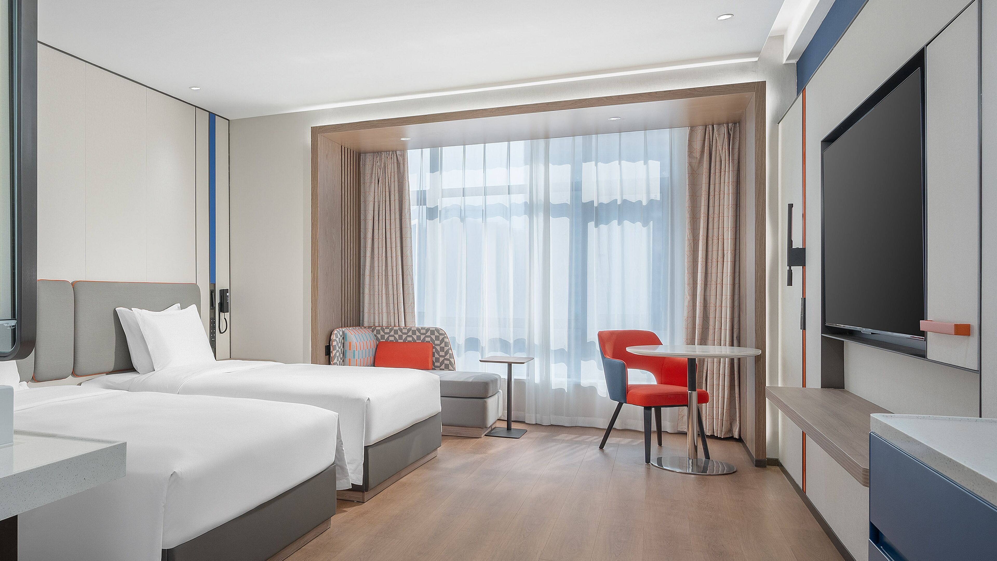 Ein Hotelzimmer mit zwei Betten, einem kleinen Tisch, einem roten Sessel und einem Fernseher.