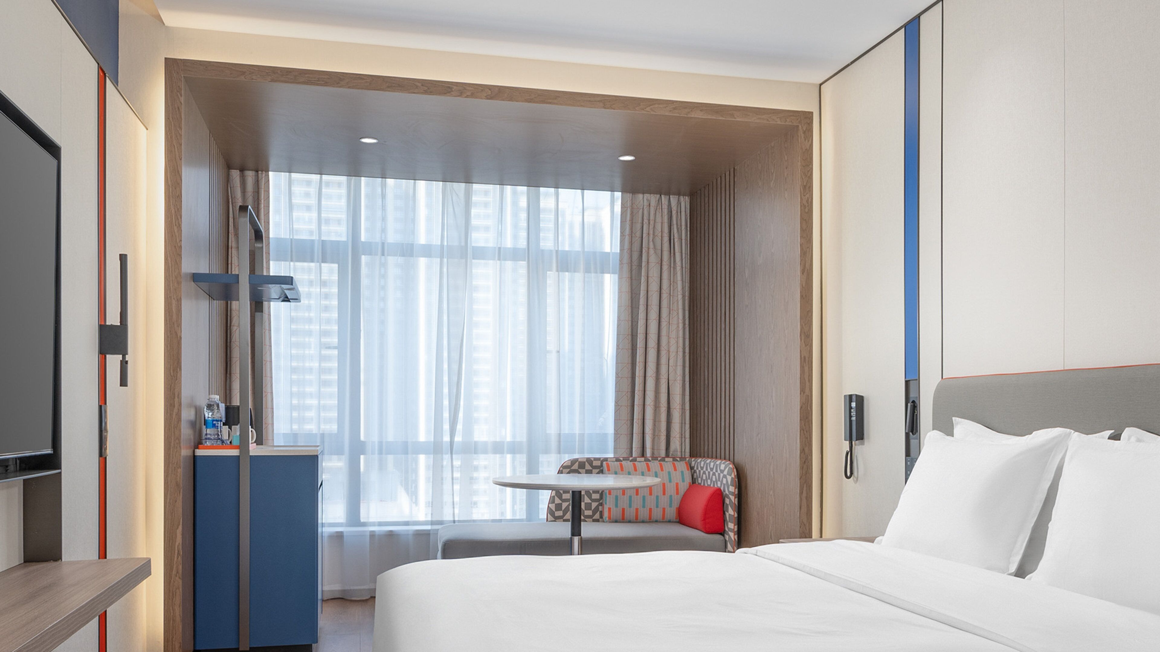 A hotel room with a large bed, a desk, a chair, and a window with curtains.
