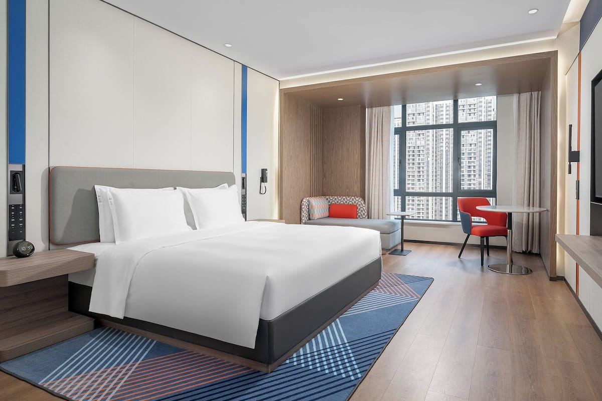 A modern hotel room with a large bed, a desk, a chair, and a TV.