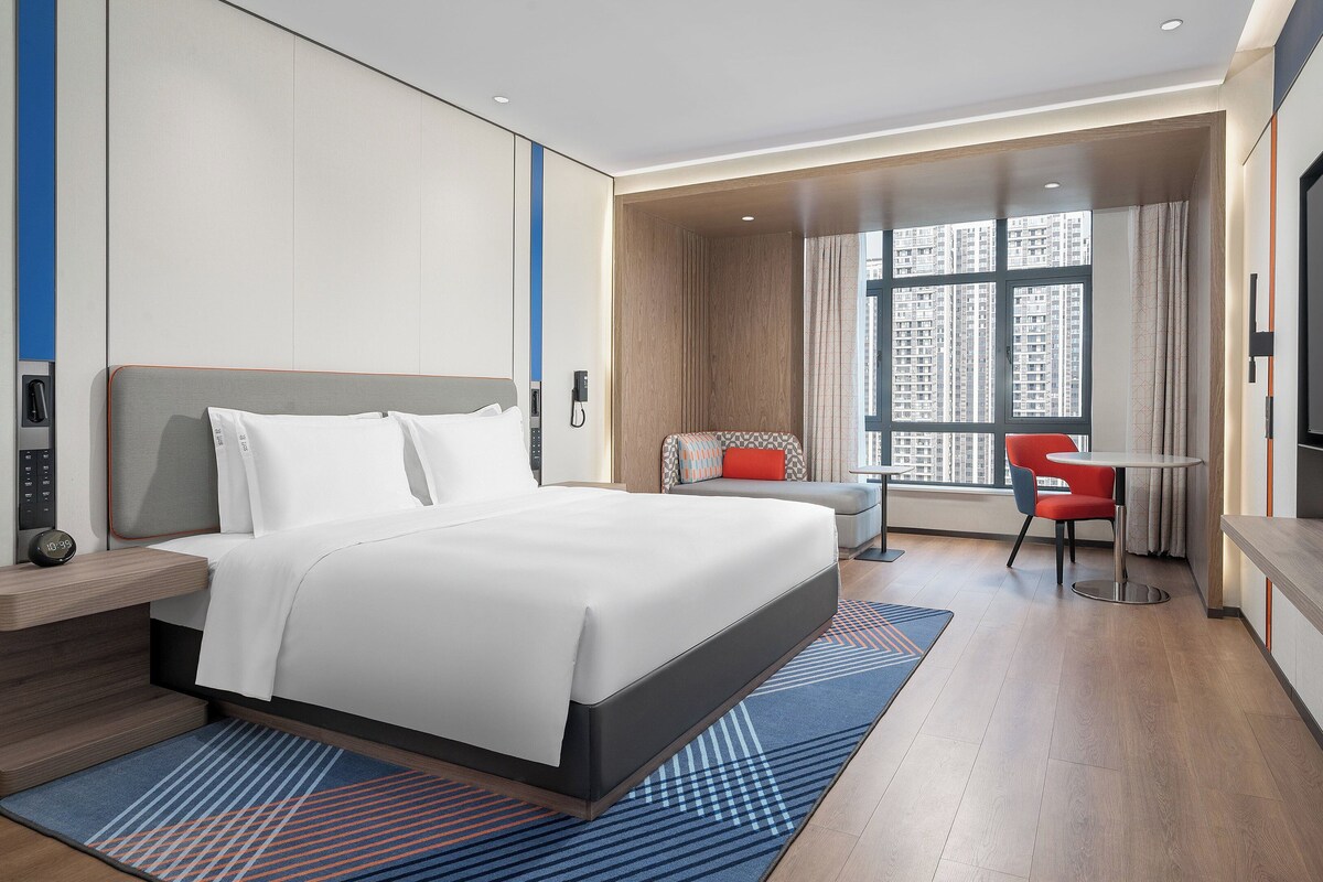 Ein modernes Hotelzimmer mit einem großen Bett, einem Schreibtisch, einem Sessel und einem Fernseher.