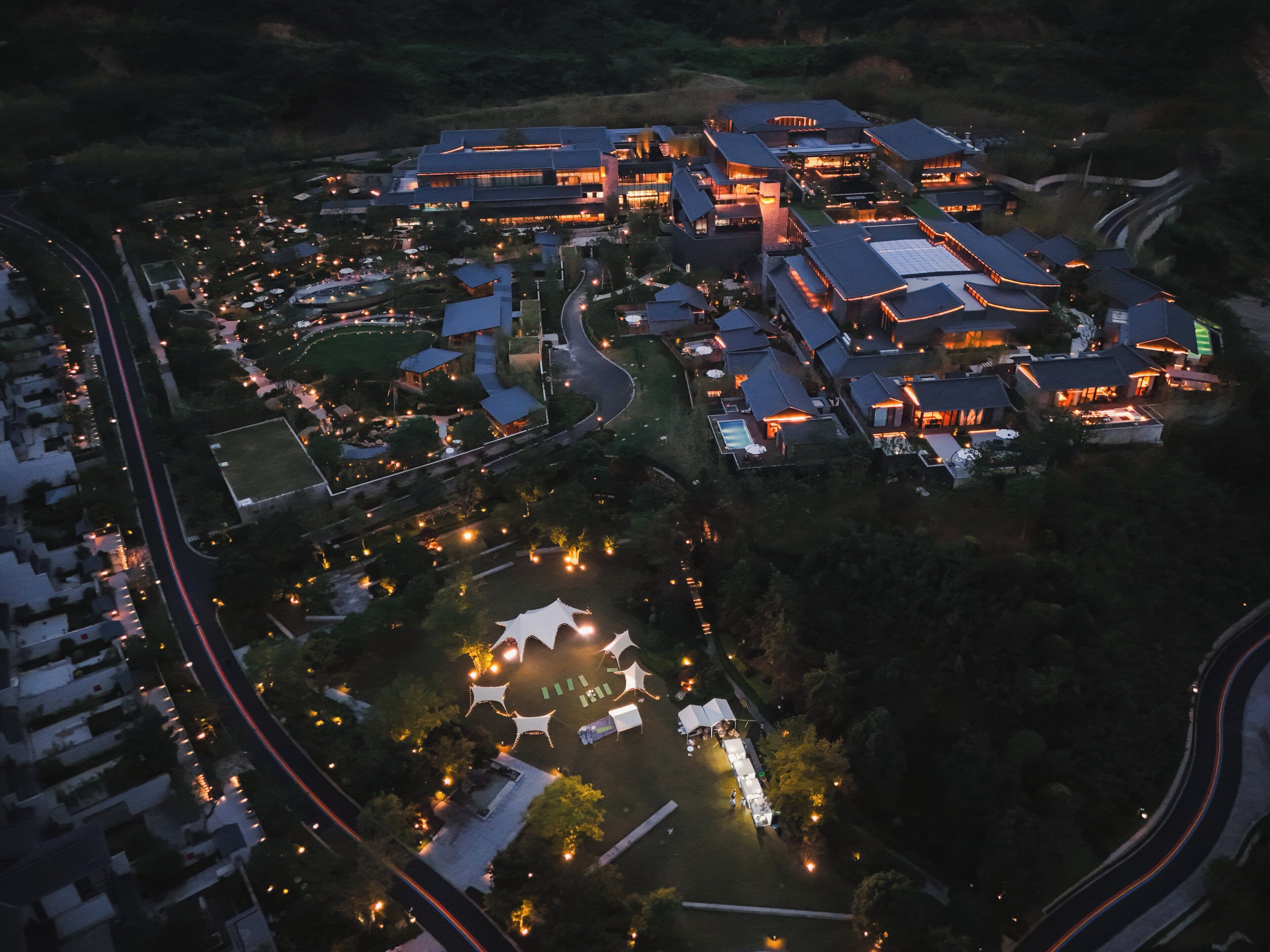 Luchtbeeld van een resort met meerdere gebouwen, een zwembad en verlichte paden.