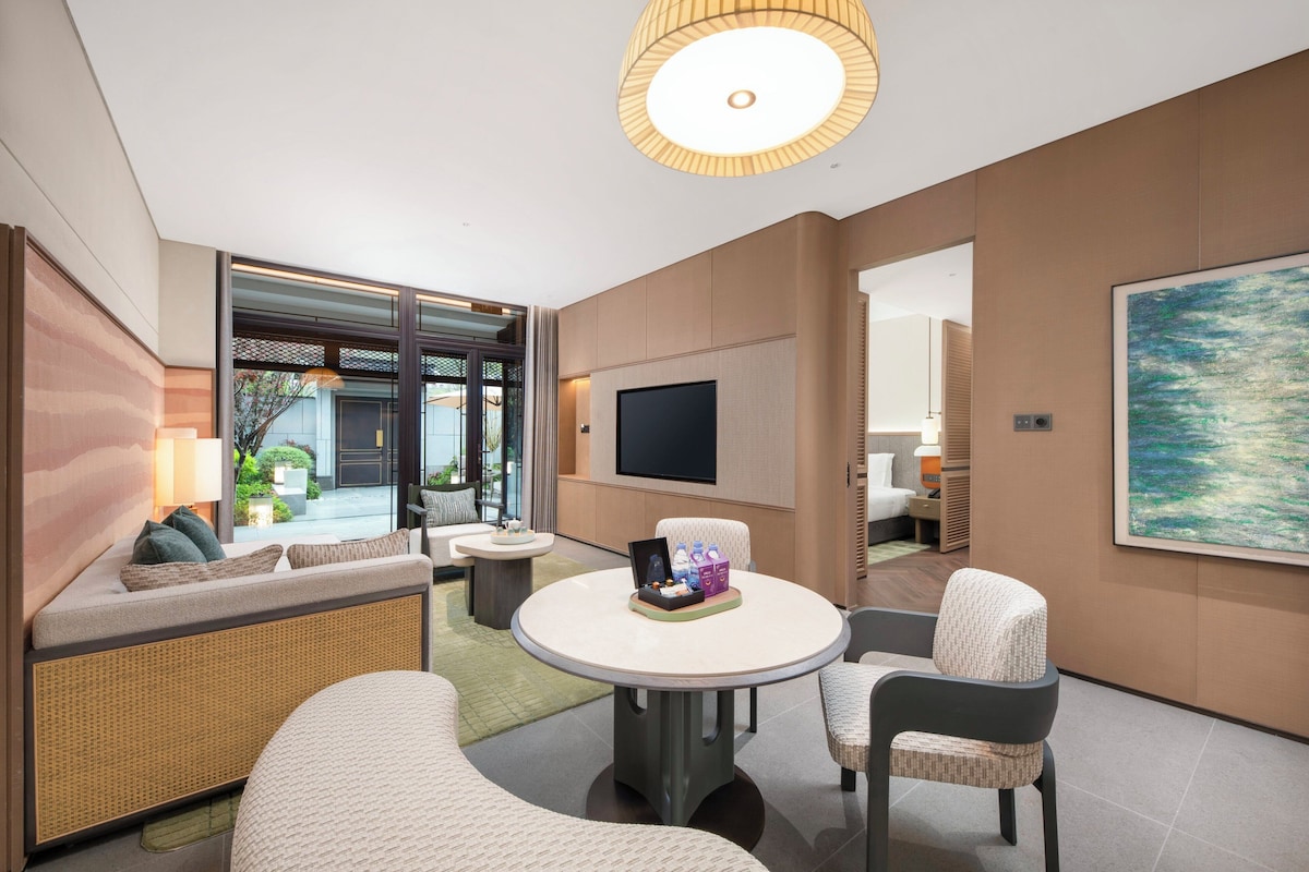 Un salon moderne avec un canapé, des fauteuils, une table ronde, un téléviseur et un grand tableau.