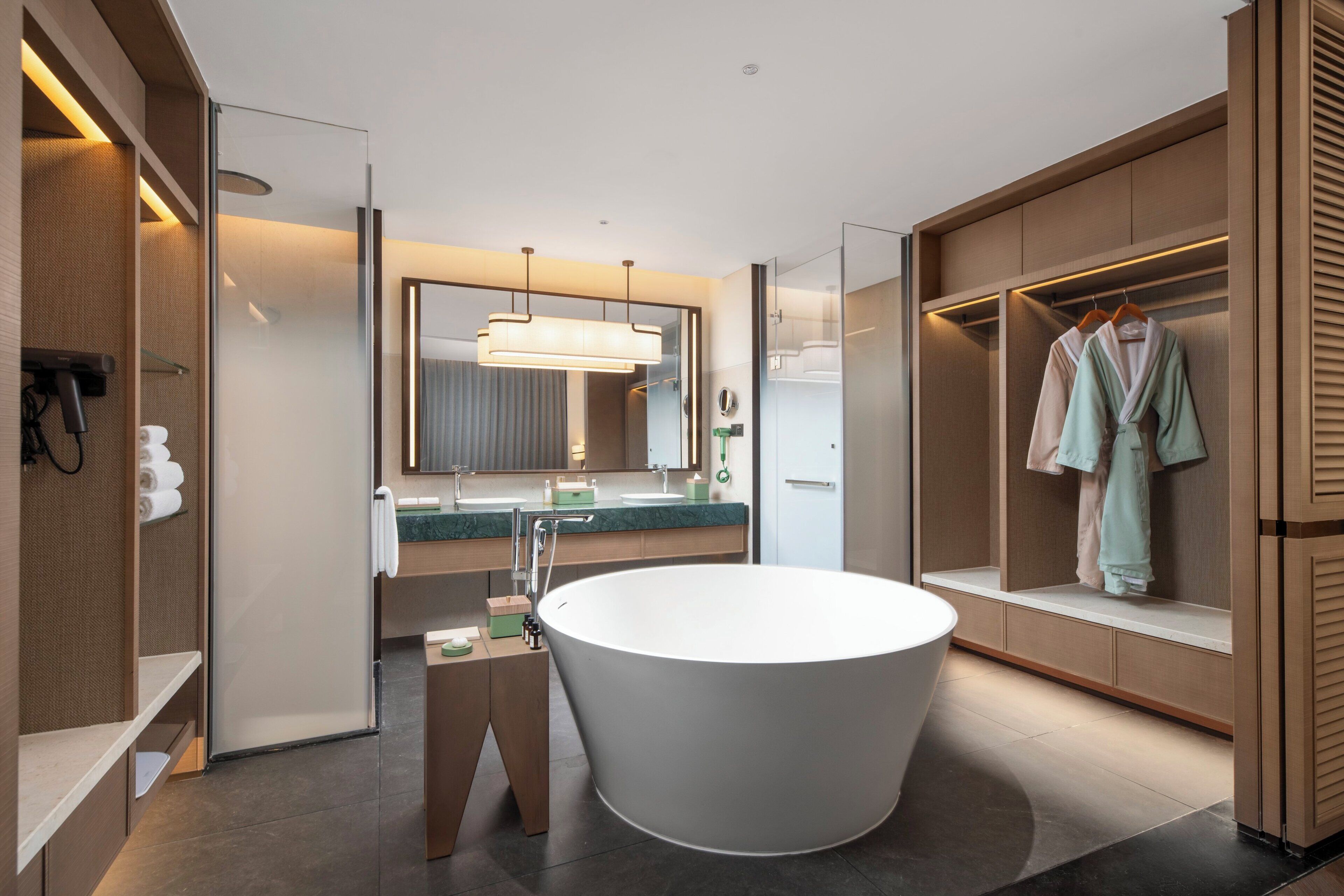 A modern bathroom with a freestanding bathtub, a vanity with a mirror, and a walk-in closet with hanging clothes.