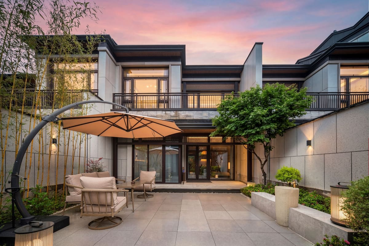 Una casa moderna con un patio, mobiliario exterior y un gran paraguas.