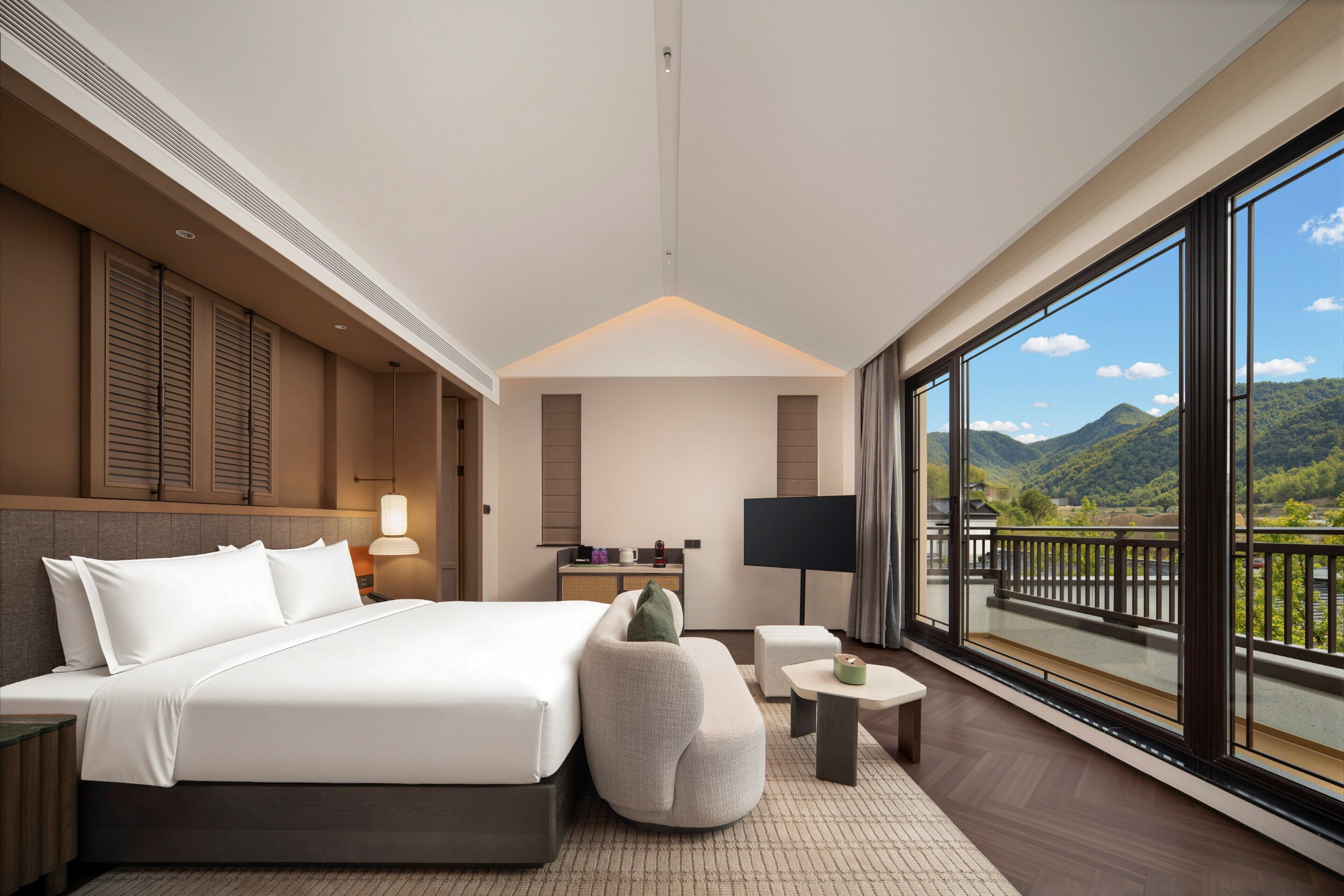 A hotel room with a bed, a desk, a TV, and a balcony with a mountain view.
