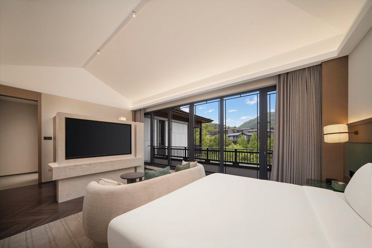 Une chambre d’hôtel dotée d’un grand lit, d’un téléviseur à écran plat fixé au mur, d’un balcon offrant une vue sur les environs et d’un aménagement intérieur moderne.