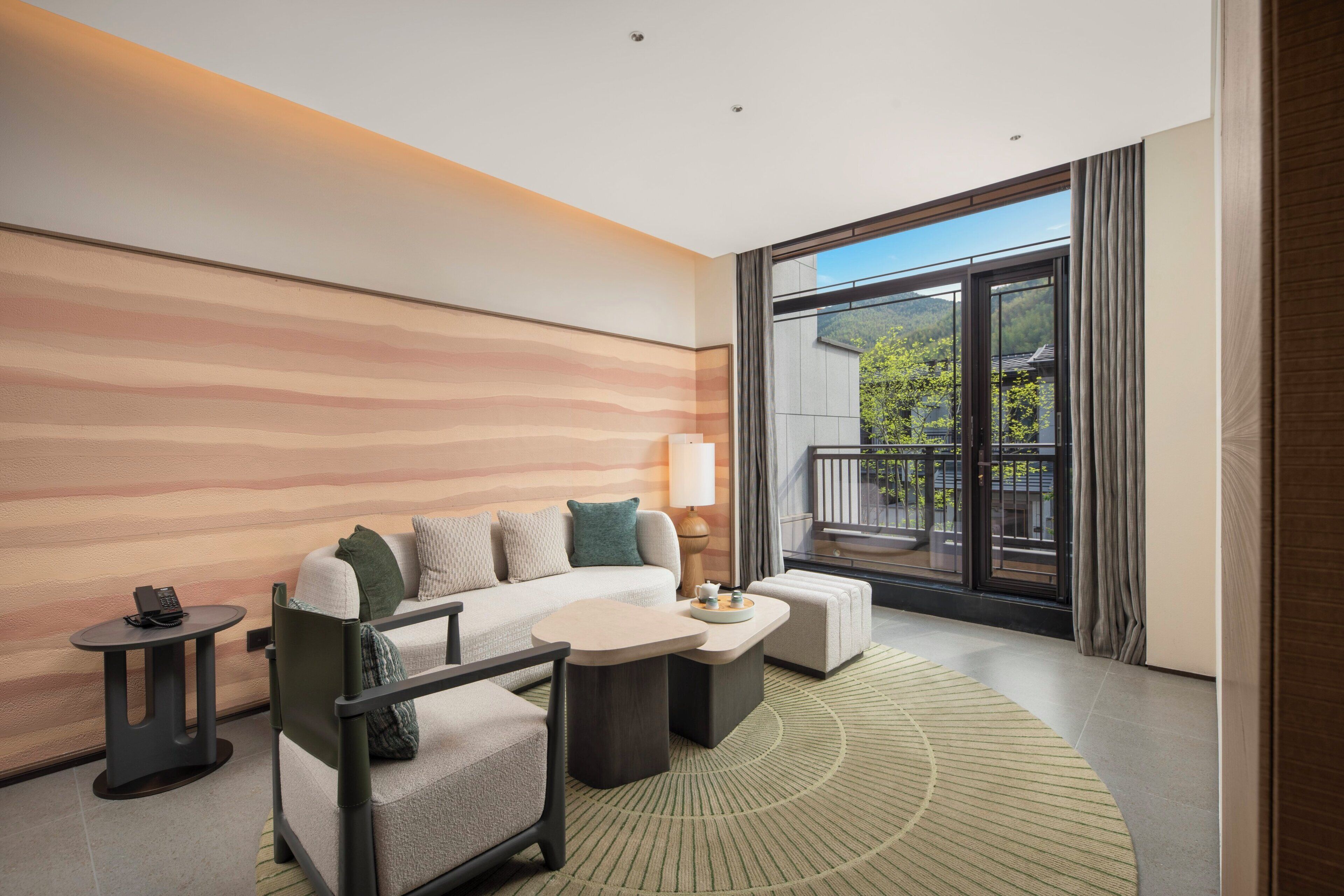 A modern hotel room with a sofa, armchair, coffee table, and a small side table.
