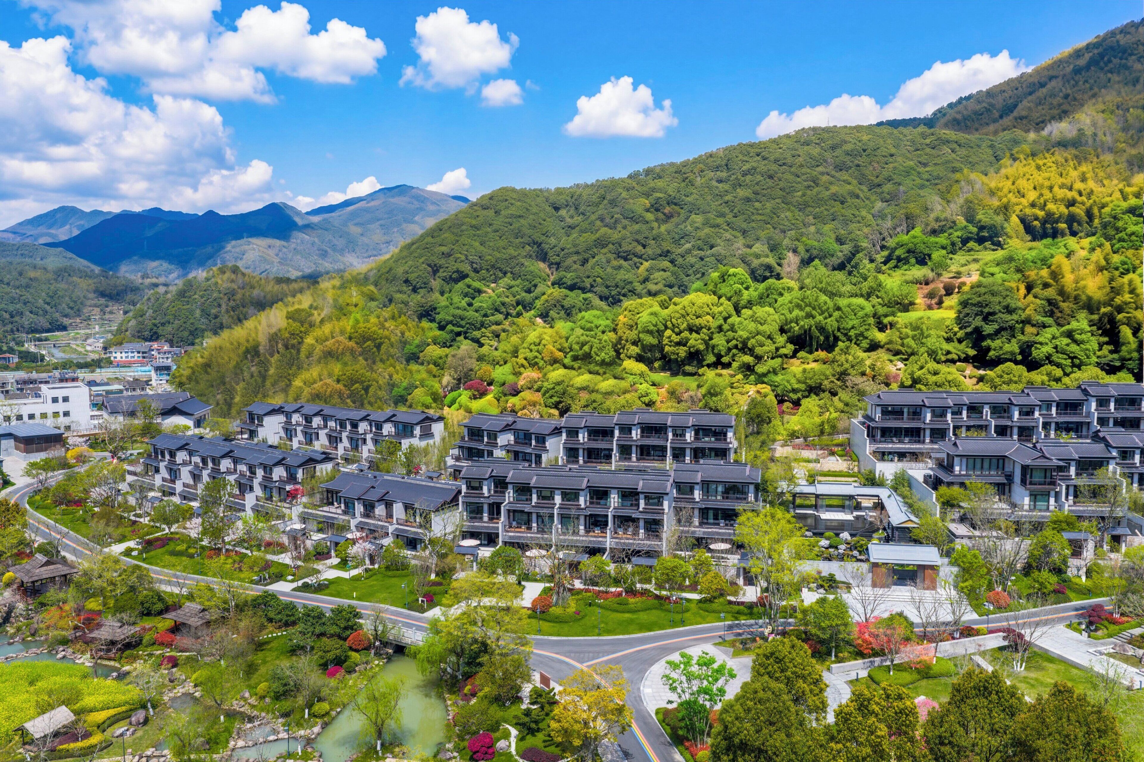 Un barrio residencial con edificios de apartamentos modernos, una carretera sinuosa y colinas verdes exuberantes al fondo.