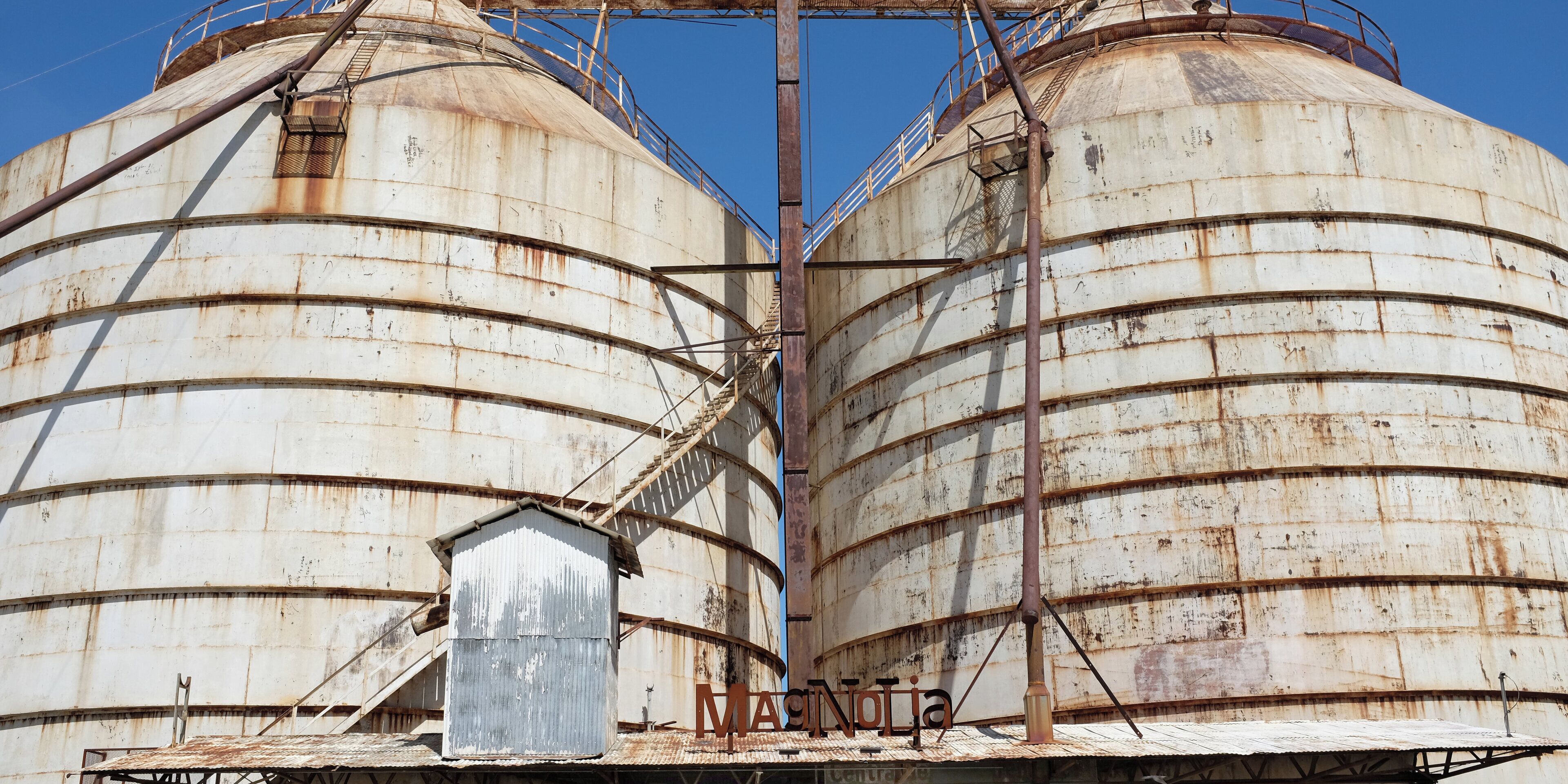 Dos silos industriales grandes y oxidados, con una pequeña estructura metálica al frente.