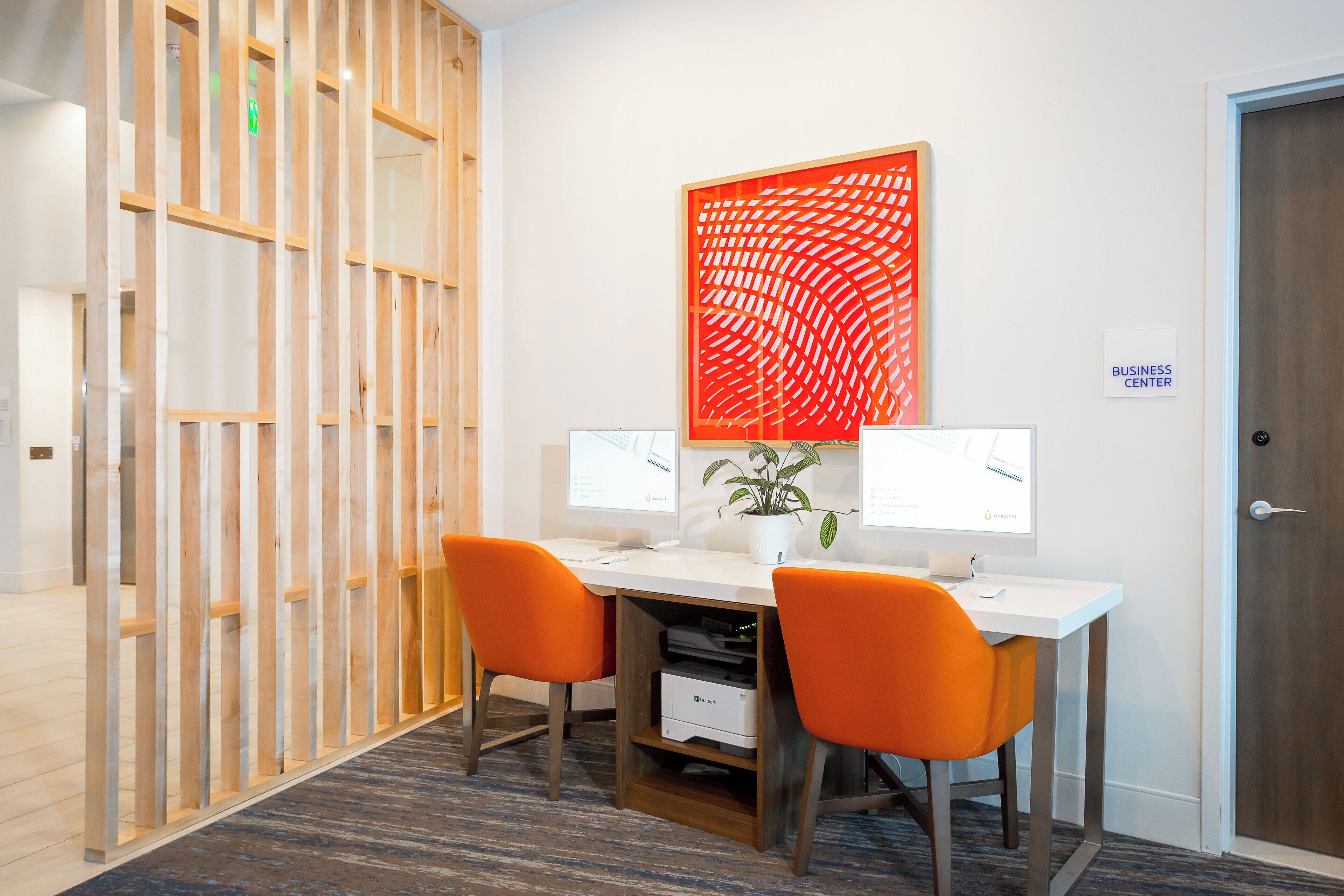 A workspace with two desks, each with a computer monitor, two orange chairs, and a potted plant.