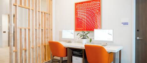 A workspace with two desks, each with a computer monitor, two orange chairs, and a potted plant.