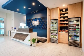A reception area with a reception desk, a wall-mounted computer, a refrigerator stocked with beverages, and a shelf with snacks. - Holiday Inn Express & Suites Waco Downtown by IHG (Waco)