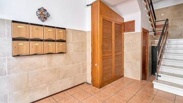 Un pasillo con suelo de baldosas, una puerta de madera, un armario empotrado en la pared y una escalera.