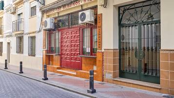 Un edificio con puerta roja, unidades de aire acondicionado y una ventana con barrotes.