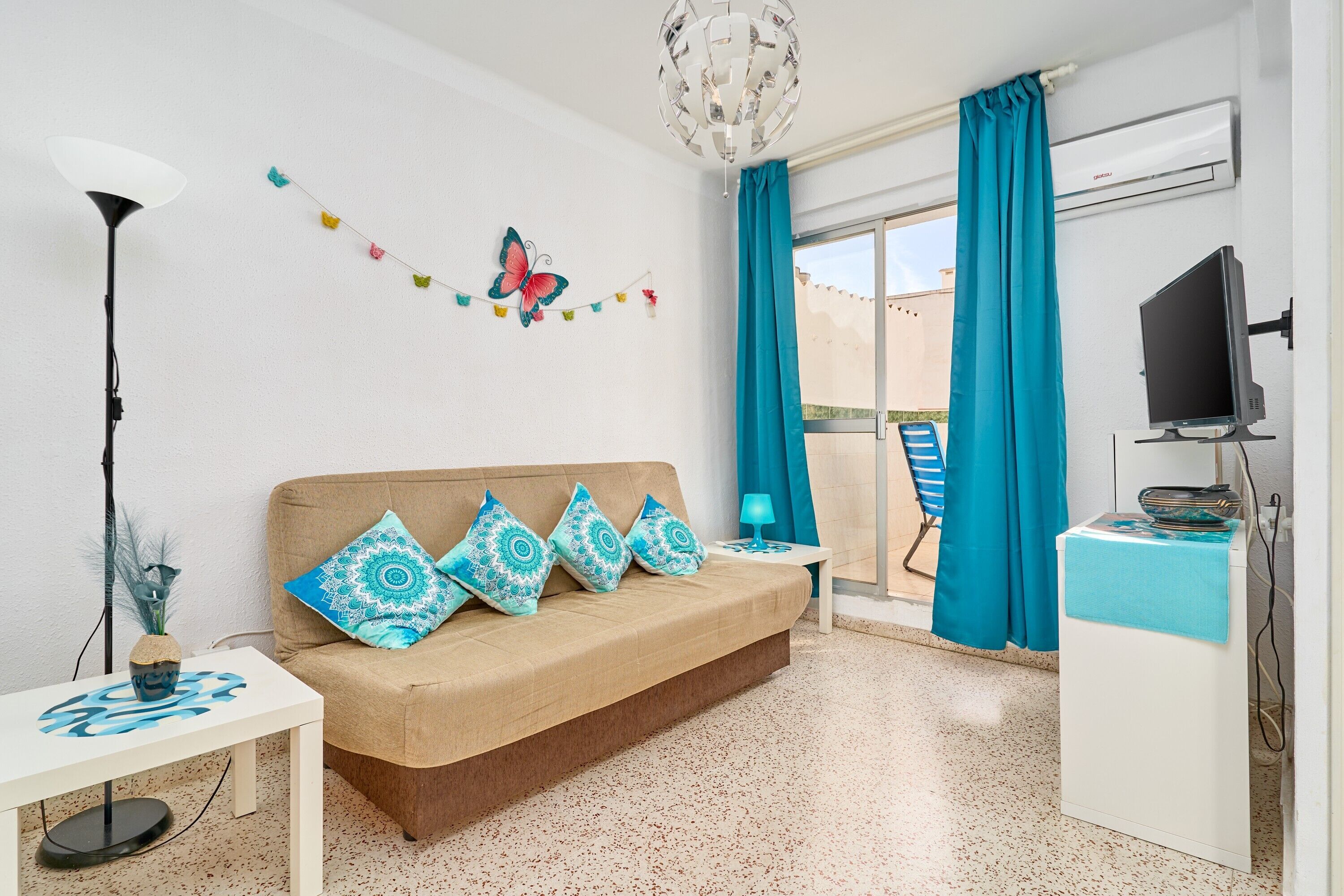 Una habitación con sofá, televisor, escritorio, lámpara y ventana con cortinas.