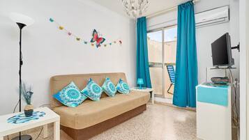 Una habitación con sofá, televisor, escritorio, lámpara y ventana con cortinas.
