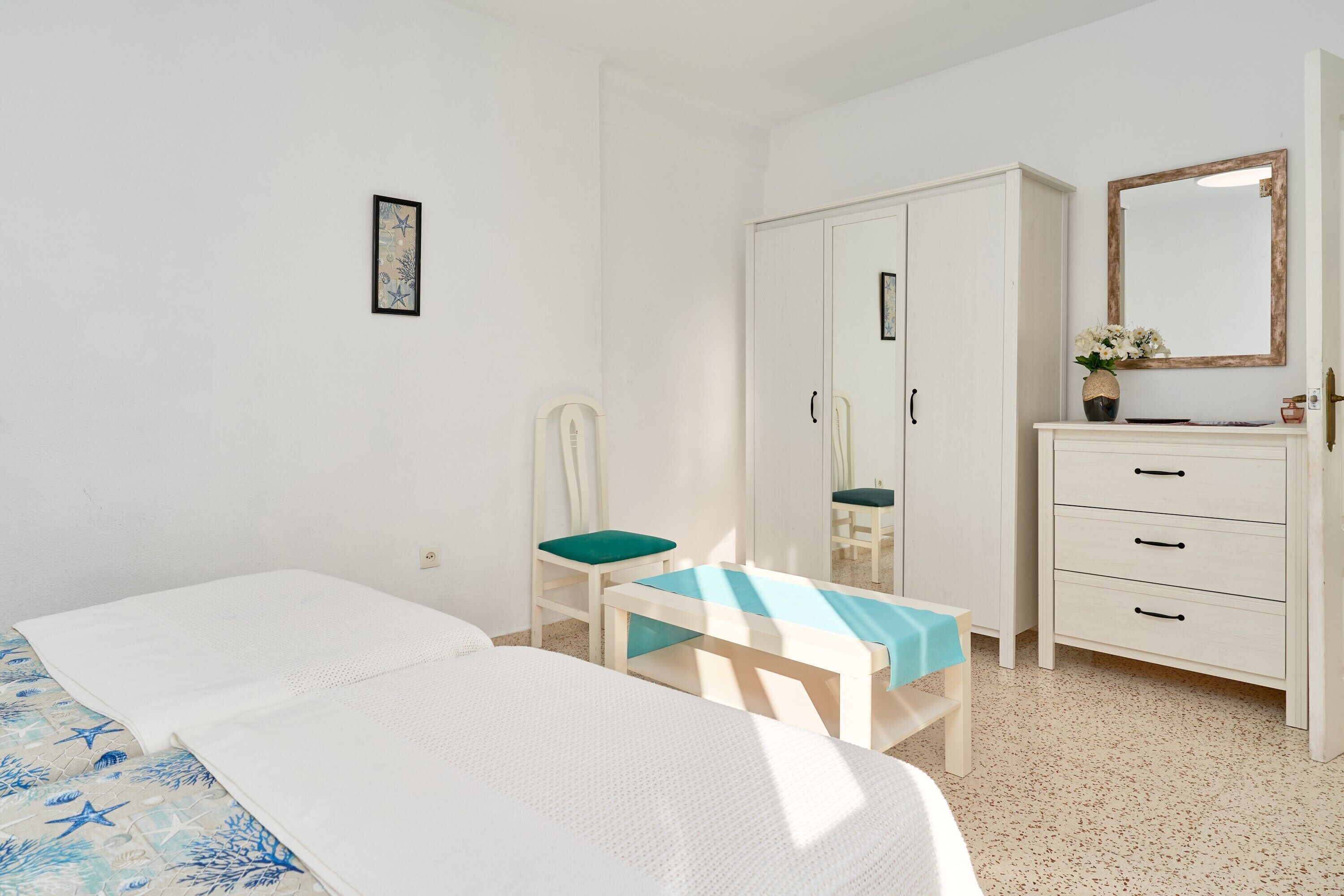 Een slaapkamer met een bed, een stoel, een bureau, een kledingkast en een spiegel.