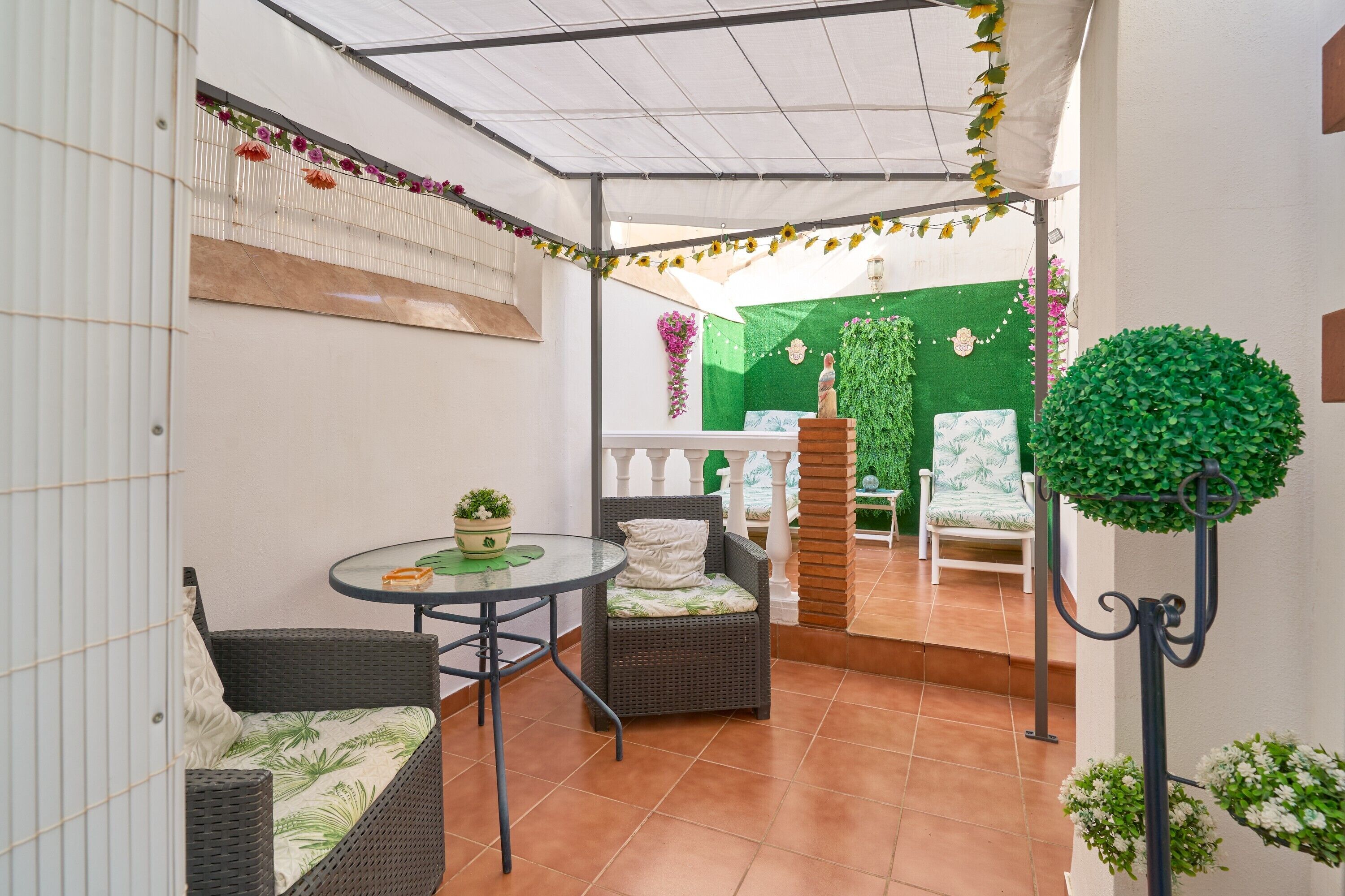 A covered patio area with wicker furniture, a small table, and a decorative plant.