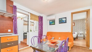 A compact room with a glass dining table, purple chairs, a bed with an orange cover, and a small kitchenette. - Apartment 'Naranja' with Private Terrace, Wi-Fi and Air Conditioning (Nerja)