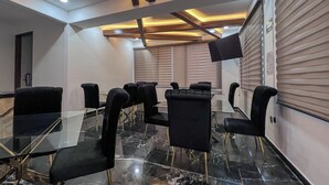 Un salón de conferencias con una mesa de vidrio, sillas negras, y un techo con vigas a la vista e iluminación empotrada.
