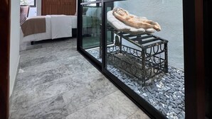 Una habitación moderna con un separador de vidrio, una cama, un armario de madera y una pequeña mesa con una escultura.