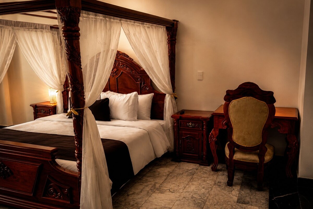 A four-poster canopy bed with a wooden headboard, a bedside table, a chair, and a nightstand.